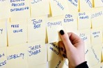 Hand reaching for a Sticky Note with a buzzword on a wall full of them.